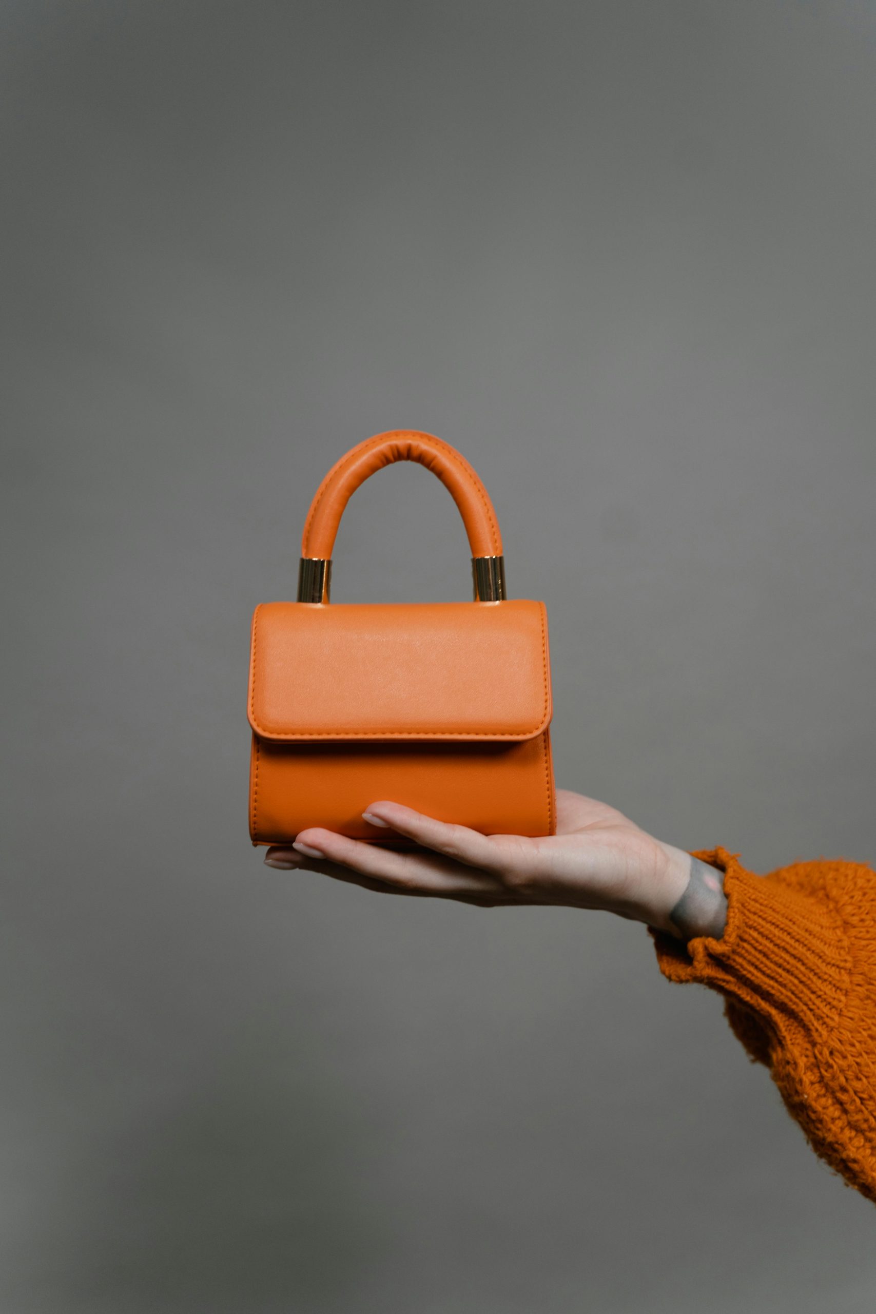 Stylish orange handbag presented on a hand in a minimalist setting, emphasizing elegant simplicity and design.